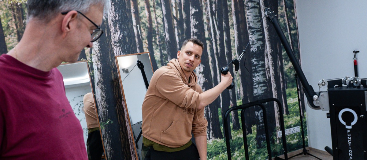 Filip „Jerry“ Stráňavský cvičí s kladkou v štúdiu pred fototapetou lesa